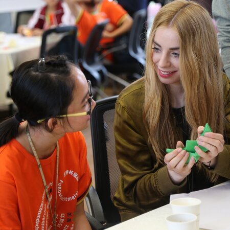 Eine deutsche und eine chinesische Schülerin sitzen an einem Tisch und sprechen miteinander