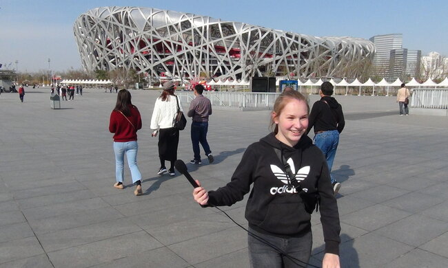 Eine Schülerin steht vor einem Sportstadion in Peking